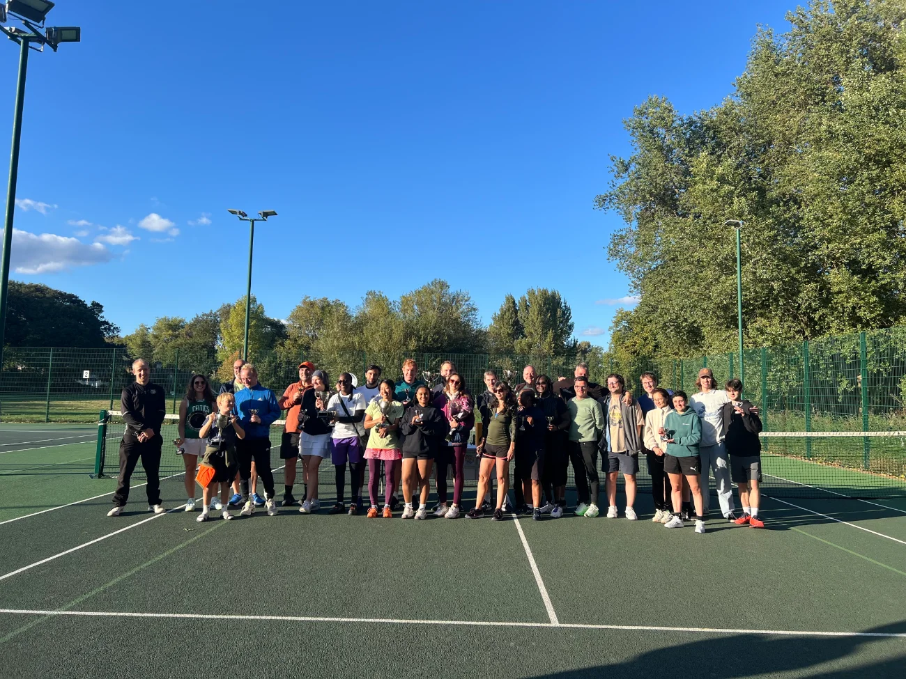 Group shot of happy tennis players on court with trophies.