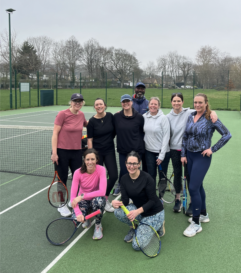 A group of smiling tennis players on court with their coach