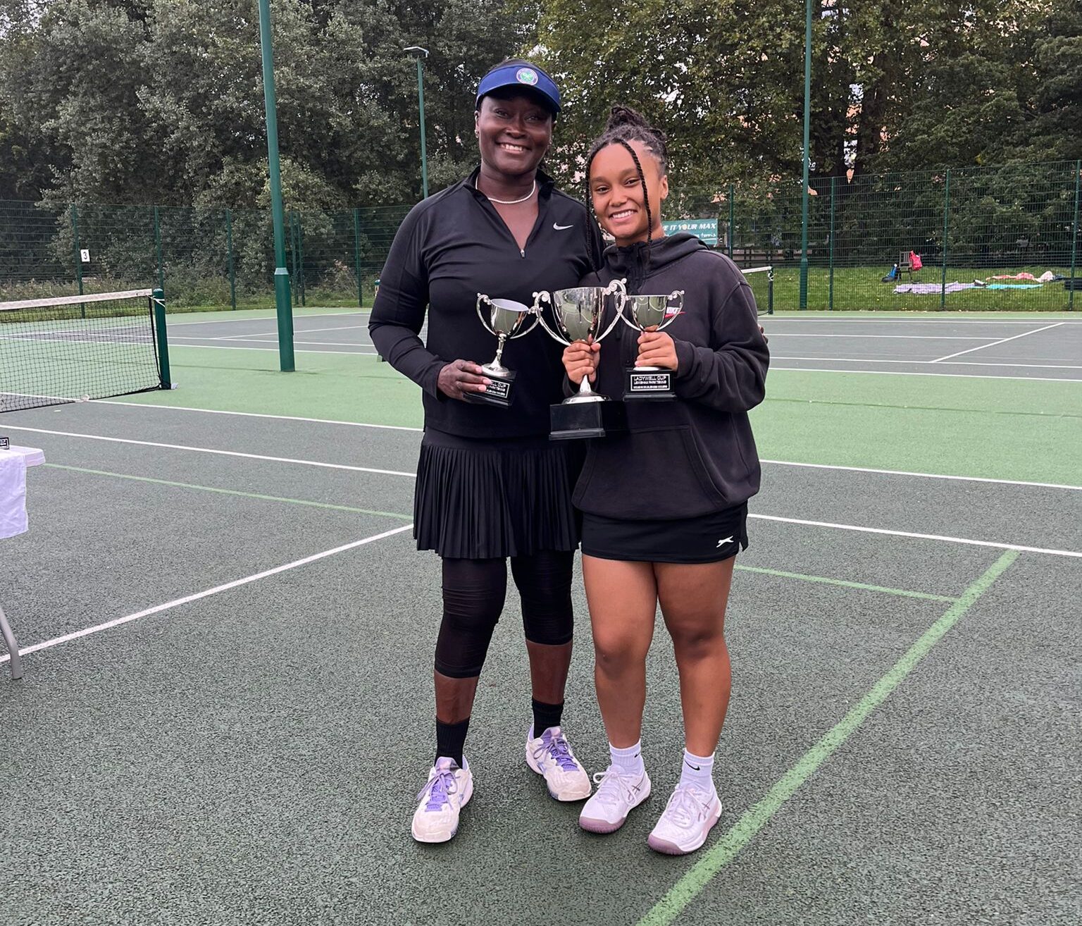 A woman and a teenage girl hold tennis trophies